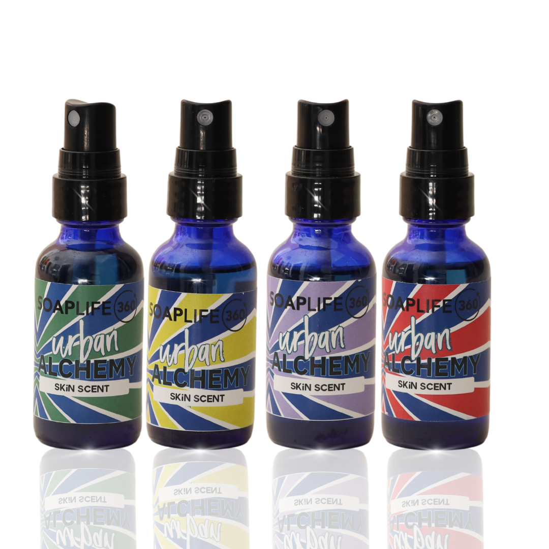 Four blue spray bottles labeled Urban Alchemy Skin Scent, with different color schemes and designs on each bottle.