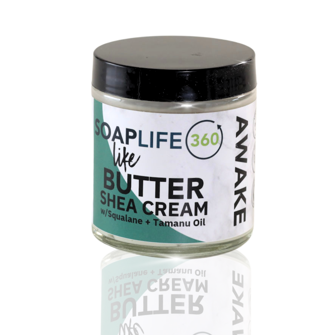 A jar of Awake Shea Butter Cream with a label that includes the brand name 'SOAPLIFE360' and the product name 'AWAKE'. The jar is clear, showcasing the white cream inside, and it has a black lid.